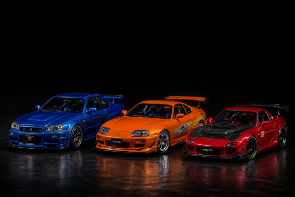 Mô hình xe hơi JDM gồm Nissan Skyline GT-R R34, Toyota Supra MK4 và Mazda RX-7 được trưng bày trên nền tối.